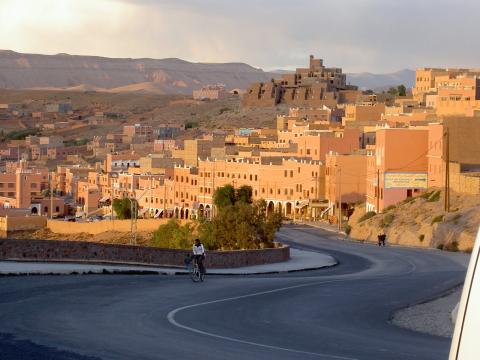 Bild eines Dorfes in Marokko in der Abenddämmerung. Im Vordergrund ist eine Strasse mit einem Velofahrer. Das Bild wurde 2004 aufgenommen.